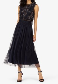 Marineblauwe jurk met kanten lijfje en geschulpte randen, doorschijnende rok met polka dots, getailleerde pasvorm en zachte textuur. Gecombineerd met marineblauwe enkellaarzen met enkelbandje.