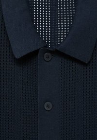 Polo de punto en color navy con un patrón texturizado y pequeños agujeros, que presenta un cuello y tres botones negros en la parte frontal.