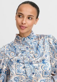 Blusa leggera blu e pesco con motivo paisley, caratterizzata da un colletto a balze, chiusure con bottoni e un design decorato.