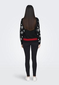 Svart tröja med vita snöflinge- och prickmönster, röd accent vid fållen; kombinerat med svarta byxor och vita sneakers.