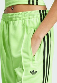 Felgroene sportbroeken met een trekkoord in de taille, voorzien van zwarte zijstrepen en een ritszak. Zwarte logo-accentdetails.