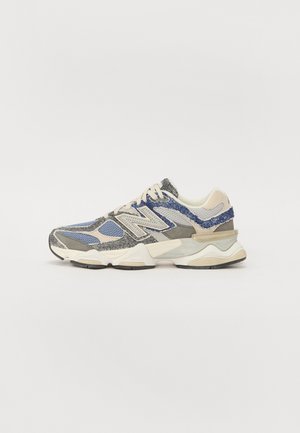 Sneaker grigia e blu con una tomaia texturizzata, realizzata in materiali mesh e sintetici, suola spessa e accenti bianchi e beige.