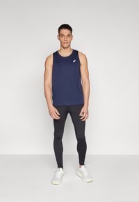 Marineblå ærmeløs atletiktop, sorte tætsiddende leggings og hvide sportsko med lime accenter. Inkluderer logo på toppen og leggings.