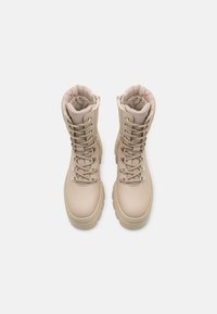 Botas beige aisladas con un diseño alto, cierre de cordones detallado, cuello acolchado y una suela gruesa para mayor estabilidad.