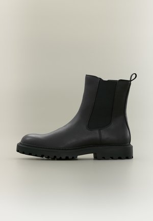 Schwarzer Leder-Chelsea-Boot mit elastischem Seitenpaneel, Zuglasche an der Ferse und dicker profillierter Sohle auf neutralem Hintergrund.