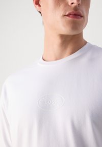 T-shirt blanc à manches longues en coton avec un logo BOSS texturé ton sur ton brodé sur la poitrine et un col rond.