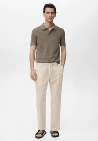 Polo shirt in olijfgroen, ribbelstructuur; lichtbeige broek met trekkoord; zwarte sandalen; eenvoudig, rechtlijnig ontwerp.