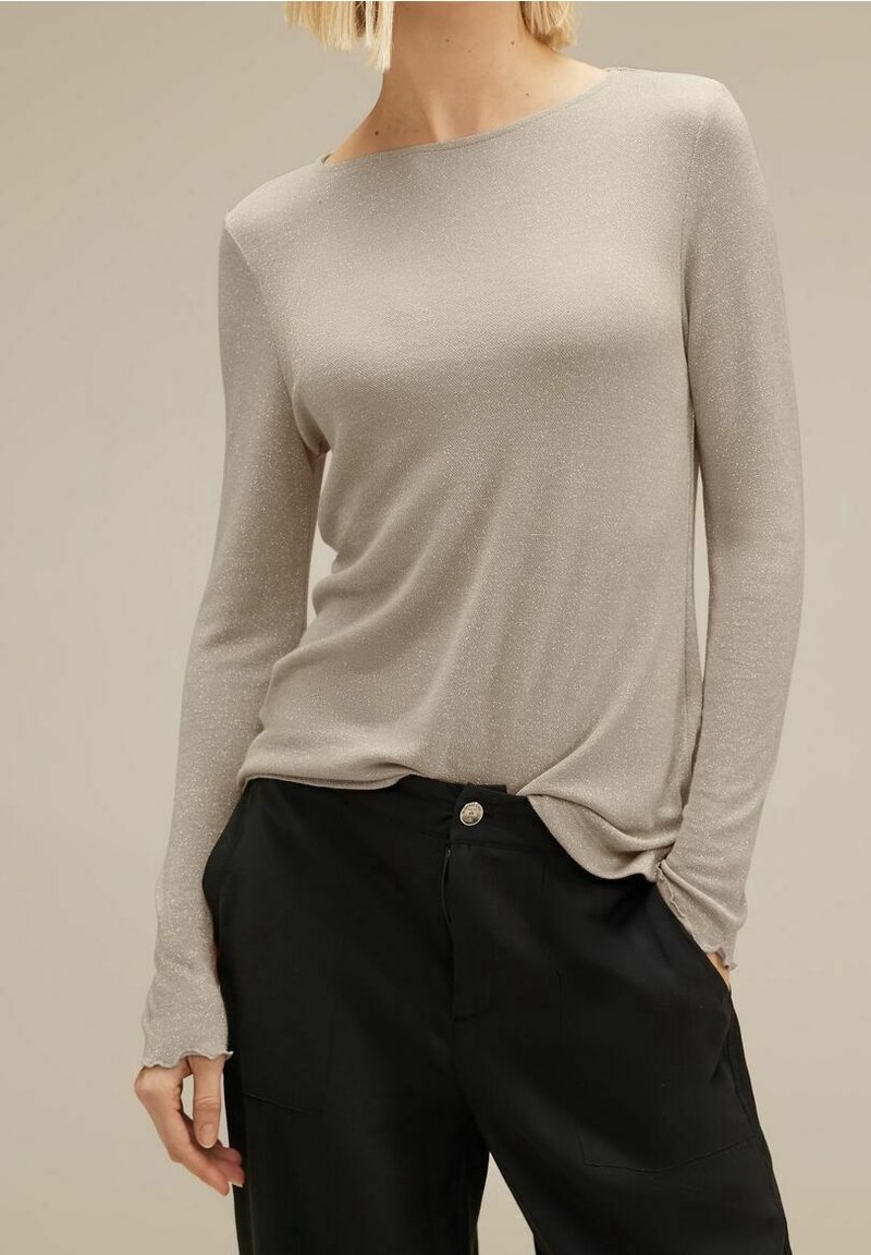 Ljusgrå långärmad topp i ett mjukt, skimrande material. Har en båtformad halsringning och en avslappnad passform, i kombination med lösa svarta byxor.