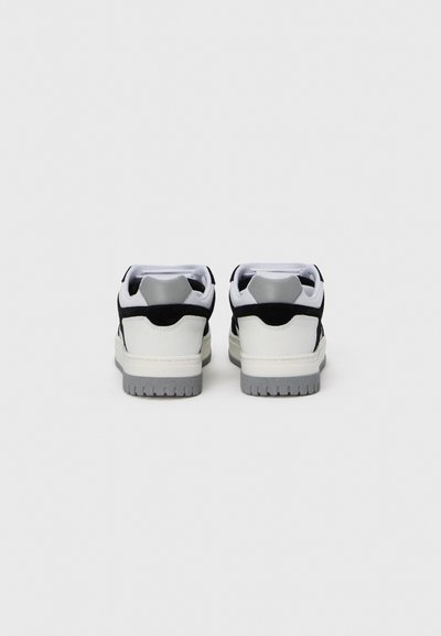 Baskets basses avec tige en cuir blanche, accents en daim noir, semelle extérieure en caoutchouc gris et col rembourré pour le soutien.