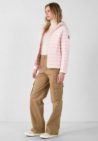 Lichtroze donsjack met capuchon, voorzien van horizontale stiksels en een logopatch, gecombineerd met beige cargobroek en witte sneakers.