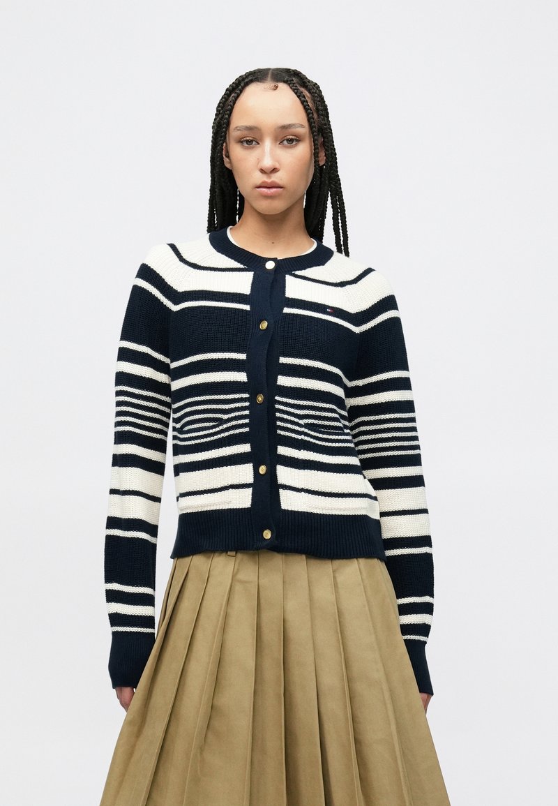 Μπλε ναυτικό και εκρού ριγέ ζακέτα με στρογγυλή λαιμόκοψη και κουμπιά στο μπροστινό μέρος. Διαθέτει πλεκτή υφή και αντίθετες ριμπ μανσέτες.