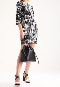 Černobílé mramorové šaty s tříčtvrtečními rukávy, černá kožená kabelka ve tvaru kbelíku a černé sandály na blokovém podpatku s bílými akcenty.