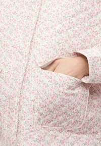 Καπιτονέ μπουφάν σε απαλό ροζ χρώμα με λουλουδάτο σχέδιο, διαθέτει μπροστινή τσέπη, υφή επιφάνειας και αντίθετο περίγραμμα στα άκρα.