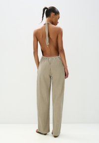 Beige trägerloser Jumpsuit mit weiten Beinen, Halsband zum Binden und elastischem Taillenbund. Strukturierter Stoff mit dezenten vertikalen Linien.
