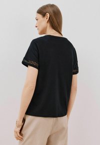 T-shirt nera a maniche corte con profilo in pizzo ai polsini. Design semplice con scollatura a girocollo e vestibilità rilassata. Tessuto leggero.
