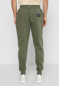 Pantalones de chándal verde oliva con cintura ajustable, piernas ajustadas y un bolsillo trasero con una etiqueta de la marca. Fabricados en un suave tejido texturizado.