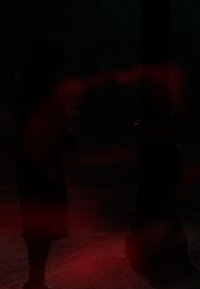 Silhouette di una figura che indossa un cappotto scuro, in piedi vicino a un lampione nero. Lo sfondo è caratterizzato da tonalità rosse sfocate e un'illuminazione tenue.
