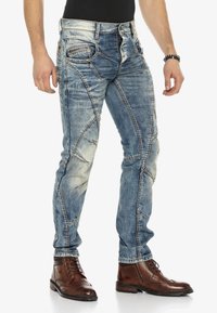 Verblasste blaue Denim-Jeans mit kontrastierenden Nähten, einzigartigem Panele-Design und vorderen Taschen, ergänzt durch braune Lederstiefel bis zu den Knöcheln.