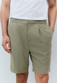 Khaki shorts made of textured fabric with a relaxed fit, featuring an elastic waistband and side pockets, ending above the knee.