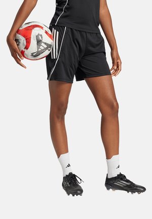 Black athletic shorts with white stripes, paired with black soccer cleats and white socks. The person holds a red and white soccer ball.