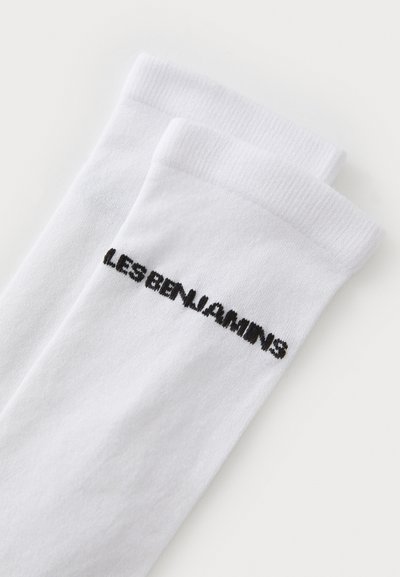 Chaussettes en coton blanches avec des bords côtelés, ornées du texte brodé noir "LES BENJAMINS" sur le côté. Texture lisse, longueur mi-mollet.