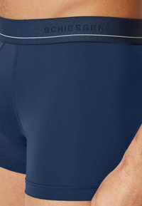 Boxer briefs blu navy con una texture liscia, vita elastica con il nome del marchio "SCHIESSER" in lettere in rilievo e una striscia bianca a contrasto.