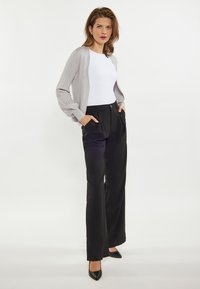 Lichtgrijze ribgebreide cardigan over een witte aansluitende top, gecombineerd met zwarte wijde broek en zwarte puntige hakken. Eenvoudig, modern ontwerp.