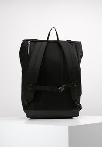 Mochila negra con respaldo de malla, correas ajustables, cierre de cremallera y detalle de hebilla. Hecha de material duradero con un diseño estructurado.