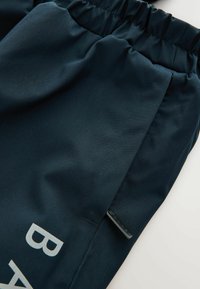 Dunkelblaue Hose mit elastischem Bund, seitlicher Tasche und einem sichtbaren kleinen Markenetikett nahe der Taschennaht.