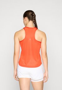 Rød mesh atletisk tank top med racerback-design, der har en glat tekstur og kontrasterende hvide accenter på ryggen. Parret med hvide shorts.