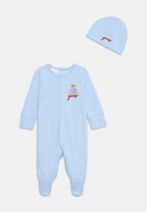 Body bébé bleu clair avec boutons-pression et bonnet assorti, tous deux brodés d'un ours en peluche et du texte rouge « "guess" ».