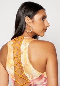 Top sem mangas multicolorido com um detalhe de rendas laranja entrelaçadas nas costas, com uma textura suave e decote redondo.