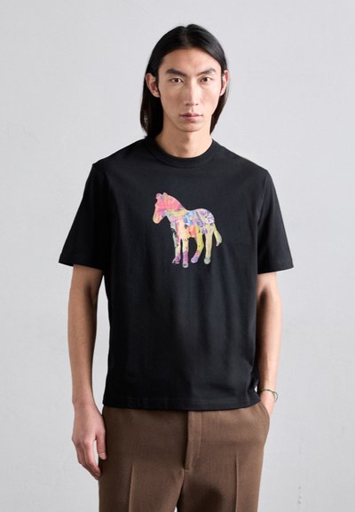 T-shirt en coton noir avec un graphique de cheval coloré et abstrait au centre. Manches courtes, col rond et coupe décontractée.