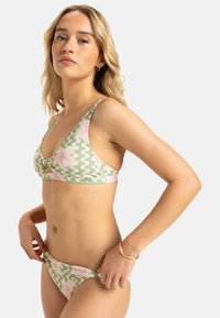 Bikini set v zelenej a ružovej vzorovanej látke, obsahujúci trojuholníkový top s uzlom a zodpovedajúce nízko-riedke spodky, vyrobené z hladkej látky.