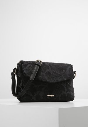 Sac bandoulière noir à motif floral avec sangle réglable et petit logo métallique "Desigual" sur le rabat avant.
