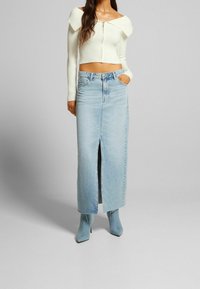 Bílé ribbované crop top s designem bez ramínek, zkombinovaný se světle modrou džínovou sukní s vysokým pasem a předním rozparkem. Modré špičaté kotníkové boty.