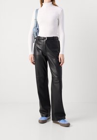 Pantalon évasé en cuir noir associé à un col roulé blanc ajusté et des baskets bleu clair. Un sac bleu clair est porté en bandoulière.