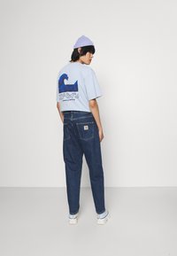  Lichtblauwe katoenen t-shirt met een golvenafbeelding op de achterkant, gecombineerd met donkerdenim jeans en witte schoenen. Inclusief een paarse beanie.