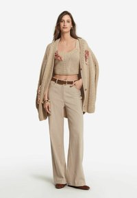 Beige stickad cardigan med blommönster, tillsammans med en figurnära beige crop top och vida beige byxor. Brun bälte och matchande skor.