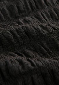 Schwarzer Textilstoff mit gekräuseltem Muster; hergestellt aus leichtem Material; weist eine weiche, zerknitterte Oberfläche und unterschiedliche Tiefen in den Falten auf.