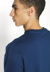 Navy blue sweatshirt with a round neckline and relaxed fit. Features a slightly textured fabric and visible stitching details at the shoulder.