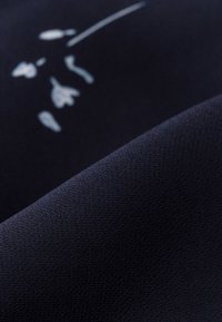 Tessuto blu navy con ricami floreali bianchi, texture soffice, superficie liscia e una leggera lucentezza, che evidenzia i dettagli delle cuciture.