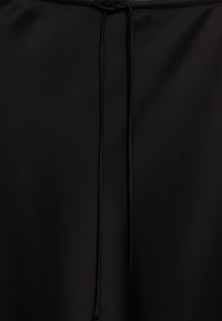 Black fabric with a centered drawstring tied in a simple knot hanging down against a smooth background.