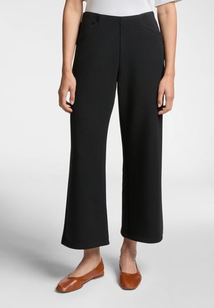 Pantaloni neri a gamba larga in un tessuto elastico, con tasche anteriori e una texture liscia. Abbinati a scarpe basse marroni.