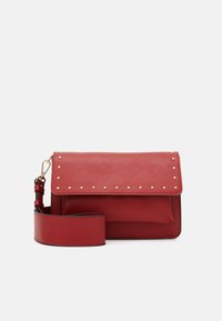 Borsa a tracolla rossa in pelle con borchie dorate sul risvolto e ampia tracolla regolabile con chiusura dorata su sfondo bianco.