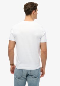Weißes Baumwoll-T-Shirt mit klassischem Rundhalsausschnitt, kurzen Ärmeln und normaler Passform, kombiniert mit hellblauen Jeans, von hinten gesehen.