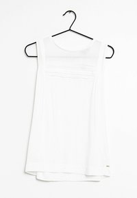 Top blanco sin mangas hecho de una tela ligera, con una textura suave, escote redondeado y un sutil detalle bordado en el pecho.