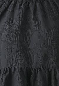 Svart klänning med strukturerad blommönsterbroderi. Tyget har en lätt glans med en rynkad volang längst ner och en slät finish.