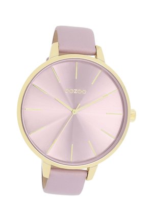 Montre métallique rose avec un boîtier doré, un cadran minimaliste, des index en or et un bracelet en cuir rose clair. Le design présente une texture en éclat de soleil.