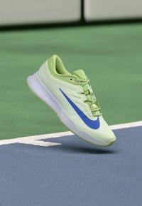 Limegrüner Sportschuh mit strukturiertem Obermaterial, blauer Swoosh-Akzent und weißer Sohle, entworfen für Höchstleistungen auf Spielflächen.